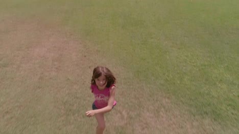 Young-girl-kid-running-in-green-field-chasing-drone-camera