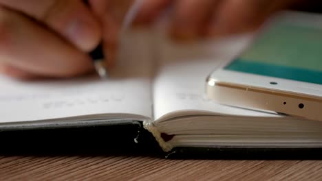 Businessman-makes-notes-in-a-notebook.-Man-writes-a-pen-in-daily.-Smartphone.-A-person-makes-notes-in-the-organizer.
