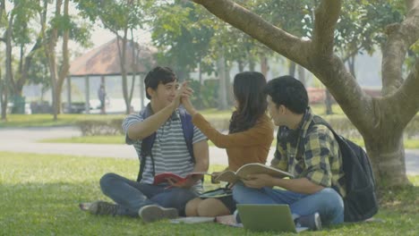 Group-of-young-students-friends-sitting-and-talking-outdoors-while-reading-book-in-university-park.