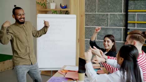 Happy-african-american-man-dancing-and-celebrating-success-of-startup-project-and-giving-high-five-with-multi-ethnic-team-in-modern-office