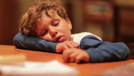 Niño-cansado-durmió-con-la-cabeza-en-la-tabla.-Joven-durmiendo-después-de-un-largo-día.-Tiro-natural-auténtico-de-vida-real-de-niño-soñoliento