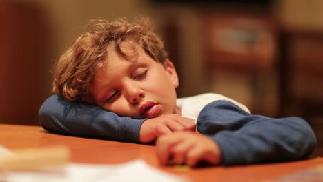 Sleepy-child-tired-fell-asleep-with-head-on-table.-Young-boy-sleeping-after-a-long-day,-exhausted-from-the-activities-of-the-day