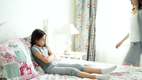 Angry-mother-argue-scolding-her-upset-little-daughter-lying-on-bed-in-bright-bedroom-at-home