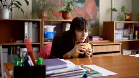 Eine-junge-Frau-in-Gläsern-versucht,-unmerklich-Hamburger-zu-essen.