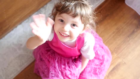 girl-in-a-pink-dress-sitting,-waving-to-camera,-view-from-above,-slow-motion