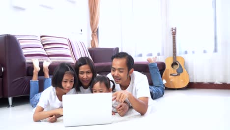 Happy-asian-family-and-little-daughter-are-lying-on-a-floor-at-home-and-using-a-laptop-computer