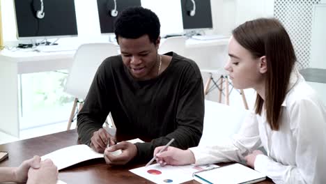 Group-of-diverse-economics-students-making-project-together.-Caucasian-girl-and-African-guy-sharing-ideas-and-taking-notes-at-team-meeting