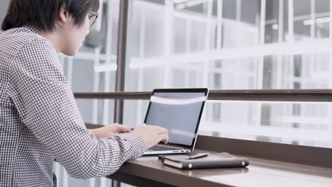 Young-Asian-business-man-using-laptop-computer-and-smartphone-on-wooden-desk-in-working-space.-Male-hand-typing-on-laptop-keyboard.-Freelance-lifestyle-in-digital-age-concept.