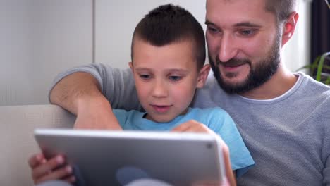 Freuen-uns-Vater-umarmt-Sohn-bei-der-Verwendung-von-Tablet-auf-sofa