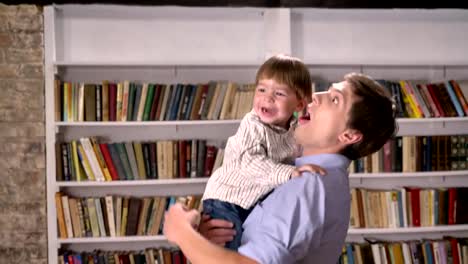 Junger-Vater-hält-seinen-kleinen-Sohn-und-springen-in-Bibliothek,-lächelnd-und-glücklich