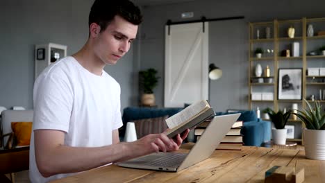 Young-Man-Reading-Book-and-Working-on-Laptop