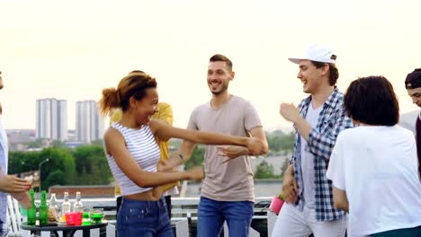 Pretty-mixed-race-girl-is-dancing-with-friends-and-laughing-enjoying-rooftop-party.-Entertainment,-partying-outdoors-and-modern-lifestyle-concept.