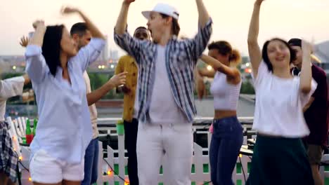 Portrait-of-men-and-women-friends-standing-with-sad-faces-at-rooftop-party-then-suddenly-starting-dancing-and-laughing.-Mood-changes,-youth-and-emotions-concept.