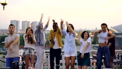 Sad-people-are-standing-on-rooftop-and-looking-at-camera-then-starting-dancing-and-jumping-having-fun-with-happy-faces-while-DJ-is-working-with-mixing-console.