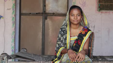 Mitte-Schuss-des-indischen-Teenager-Mädchen-sitzt-zu-Hause-mit-Sari-Kleid-anpassen-traditionelle-Namaste-Respekt-bedeckt-Kopf-Blick-in-die-Kamera-Henna-tätowiert-Hand-in-Hand-zur-Begrüßung-lächelnd-Inhalte-statisch