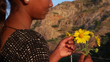 Indian-teenager-beautiful-girl-with-flowers-yellow-waiting-at-a-hill-top-under-a-tree-on-a-summer-day-in-love-happy-joy-sun-tropical-hot-bright-sunshine-content-looking-at-camera--handheld-stabilized