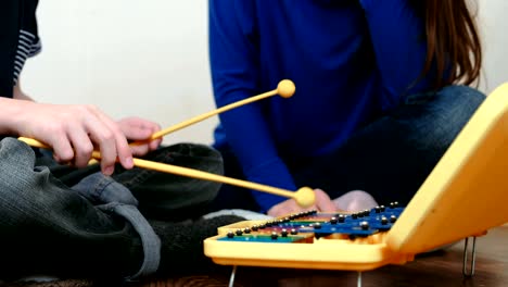 Playing-music-instrument.-Closeup-boy's-hand-playing-on-xylophone-and-his-mom-sitting-near-him.