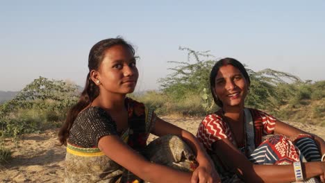 Handheld-stabilisierten-Schuss-von-zwei-Frauen-sitzen-auf-einem-Sandhügel-Wüste-an-einem-heißen-Sommertag-in-ihrer-Tradition-indische-Kleidung-Sari-Blick-direkt-auf-Kamera-und-Austausch-und-Kommunikation