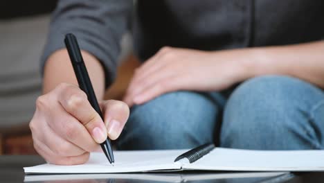 Die-Hand-einer-Frau-auf-einem-weißen-leeren-Notebook-auf-Tabelle-aufschreiben