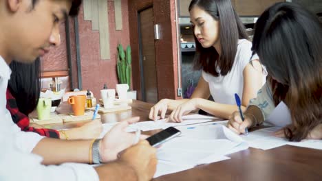 Glückliche-junge-asiatische-Studenten-studieren-und-diskutieren-mit-Büchern-und-Schreibpapier-für-Projekte