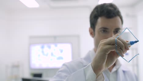 Medizinische-Forschungswissenschaftler-schreibt-wissenschaftliche-Formel-auf-einem-Glas-Whiteboard-mit-ernstem-Gesicht