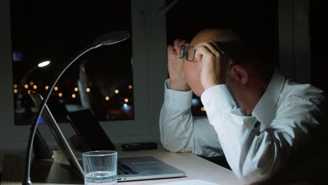 Tired-businessman-working-by-notebook-and-doing-neck-massage-in-night-office