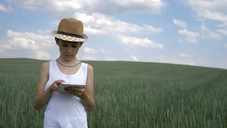 Landwirt-Junge-mit-Hut-verwendet-eine-Tablette-im-Feld,-prüft-die-Ernte