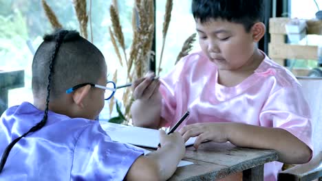 Happy-little-asian-boy-with-writing-in-notebook-and-pencils-drawing-at-home.-education-concept