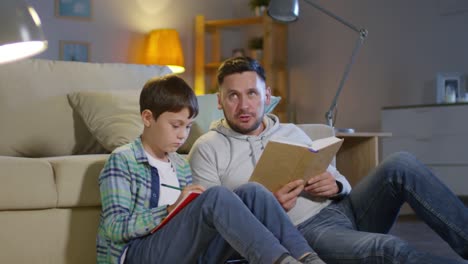 Mann-hilft-Sohn-bei-den-Hausaufgaben-im-gemütlichen-Wohnzimmer