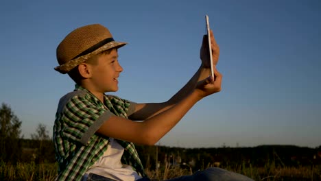 chico-en-un-sombrero-se-encuentra-en-la-parte-superior-y-habla-en-la-comunicación-de-vídeo-utiliza-una-tableta,-al-aire-libre