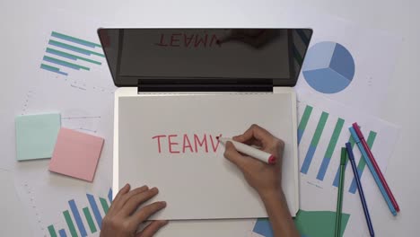 Frau-TEAMWORK-auf-ein-Stück-Papier-am-Laptop-schreiben.