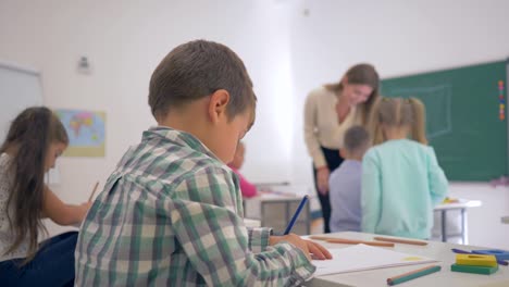 Retrato-de-sonriente-colegial-en-mostrador-durante-la-lección-de-educación-Aula-en-escuela-primaria-de-fondo-desenfocado