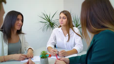 four-high-school-students-sitting-at-table-and-discussing-institute-assignment-in-library