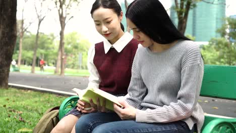 Two-young-female-friends--reading-a-book-together-in-public-park-outdoors.-Multi-ethnic-diversity.