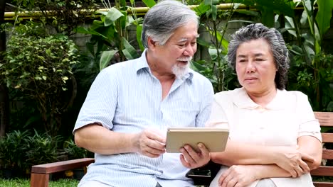 Senior-couple-sitting-and-using-tablet-together-in-home-garden.