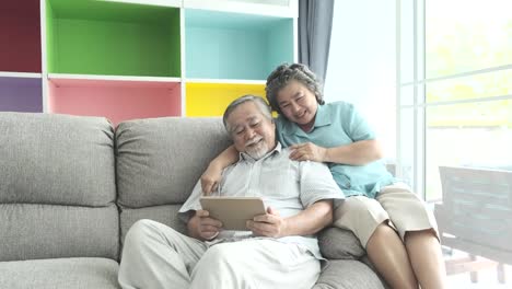 Älteres-paar-sitzen-und-beobachtete-Tablet-im-Wohnzimmer.