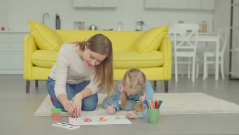 Linda-chica-con-la-madre-que-hace-de-la-pintura-en-casa