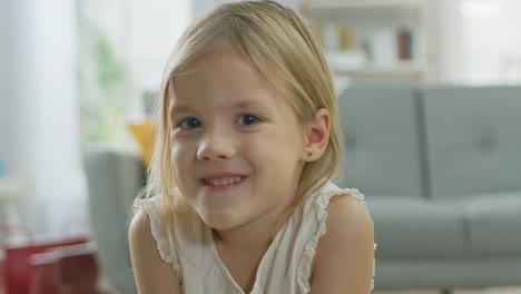 Porträt-von-süßen-niedlichen-glückliche-junge-Blonde-Mädchen-lächelnd-vor-der-Kamera.-Im-Hintergrund-unscharf-sonniges-Zimmer.