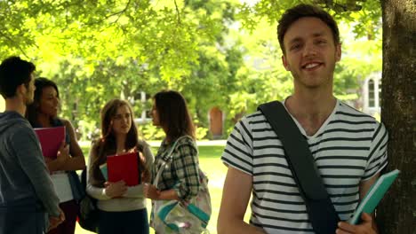 Cheerful-student-posing-and-classmates-speaking-behind-him