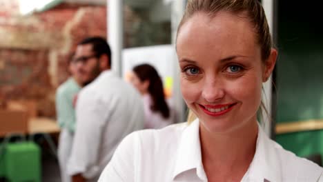 Casual-businesswoman-smiling-at-camera-with-team-behind-her