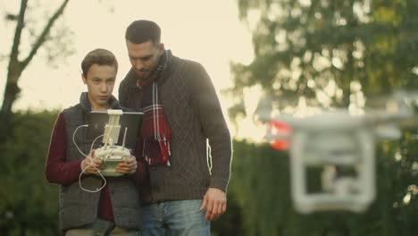 Son-Controls-Flying-Drone-while-Father-Watches.-In-the-Park.