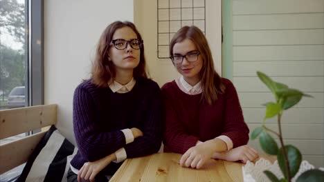 Gafas-de-los-estudiantes-de-dos-chicas-guapas-sentado-en-la-mesa-en-la-cafetería-mirando-a-cámara