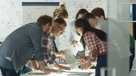 Siete-personas-con-estilo-de-pie-diversa-se-inclinan-en-una-mesa-de-conferencias-mientras-hablan-enérgicamente-de-los-planes-de-negocios-diarios.