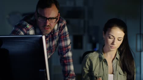 Late-at-Night-in-Engineering-Firm,-Close-up-of-a-Male-and-Female-Colleagues-Work-on-Drafts-with-the-Help-of-Computer.-Table-is-Lit-by-Lamp.