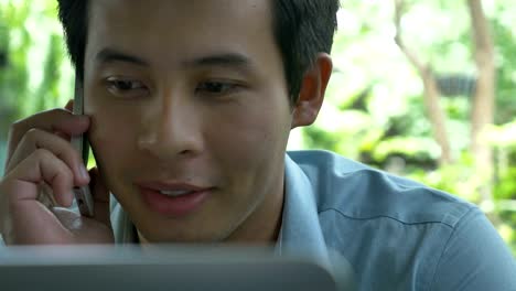 4K-:-Young-Asian-businessman-using-a-laptop-while-talking-on-mobile