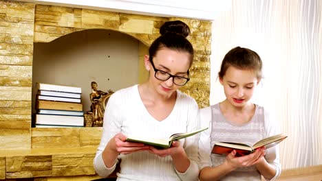 niños-sentados-juntos-cerca-de-la-chimenea-en-casa-y-leyendo-libros,-niñas-sonriendo-y-abrazando-a