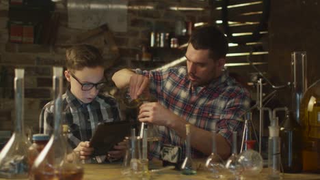 Vater-und-Sohn-machen-chemische-Experimente-während-der-Überprüfung-eines-Tablet-Computers-in-einer-Garage-zu-Hause.