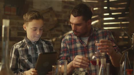 Vater-und-Sohn-machen-chemische-Experimente-während-der-Überprüfung-eines-Tablet-Computers-in-einer-Garage-zu-Hause.