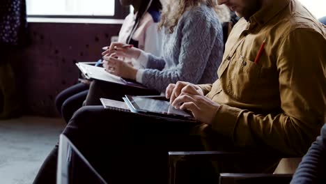 Close-up-view-of-young-multiracial-team-sit-at-business-meeting.-Man-and-woman-make-the-notes-on-tablet-and-notebook