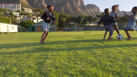 Escuela-primaria-a-los-niños-jugando-al-fútbol-en-un-campo
